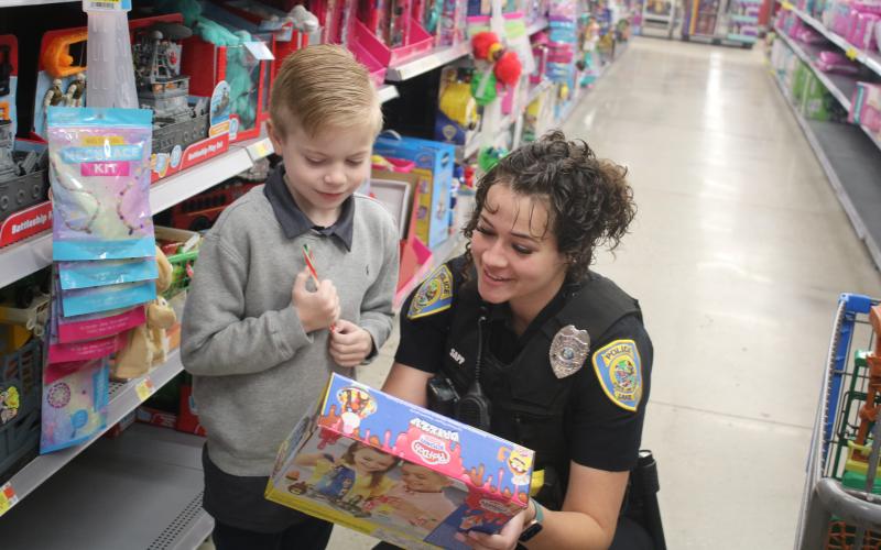 Dexter Gamble, 7, and Lake City police officer Taylor Sapp, look at the specs on a toy Gamble was considering purchasing during the Shop With A Cop event on Wednesday morning at Walmart. The Lake City Police Department has hosted the event for 10 years. (TONY BRITT/Lake City Reporter)