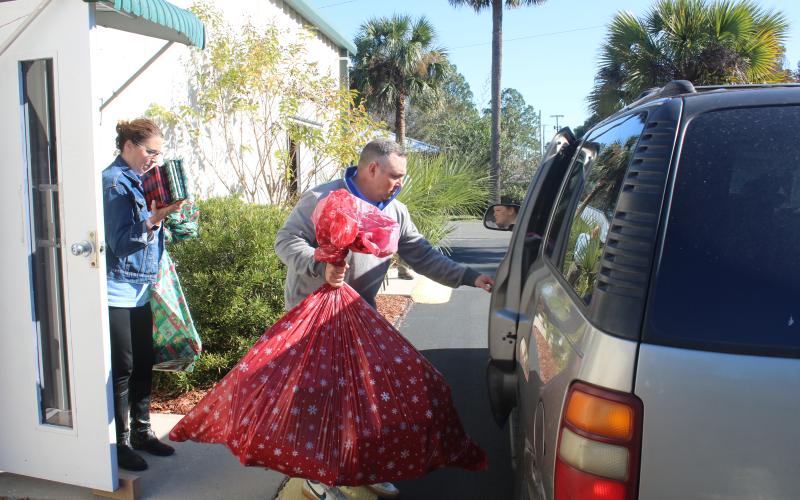 JD Curls prepares to load a bag of toys into a vehicle as Jennifer Davis brings a handful books and other items to the vehicle during the Christmas basket dispersal Monday morning at the Christian Service Center. (TONY BRITT/Lake City Reporter)
