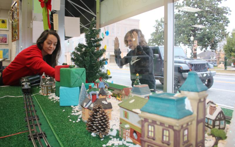 Shane McPherson, 13, of Gainesville, peers through the Gateway Art Gallery window Wednesday as his aunt, Shelia Carr, Gateway Art Gallery curator, works on a holiday display that features a holiday village with a working electric train. (TONY BRITT/Lake City Reporter)