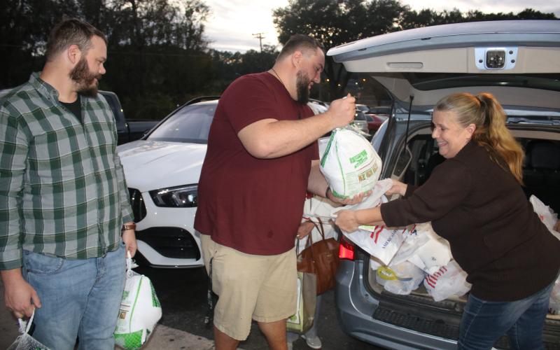 Josh Fuller (from left) and James Crenshaw pass turkeys to Dawn Johnson for the Elks Lodge Christmas baskets Thursday night. (TONY BRITT/Lake City Reporter)