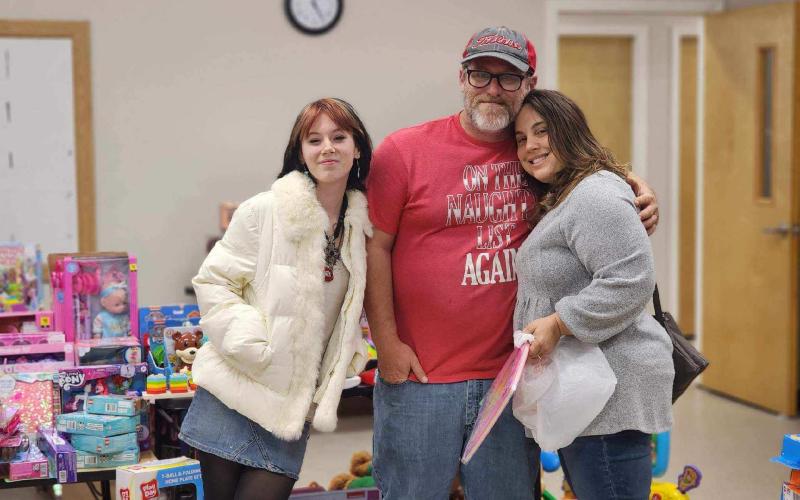 Kids Feeding Kids officials Emily Cole (from left), John Cole and Sharon Simpkins share a group hug during the organization’s ‘Miracle on KFK Street’ on Saturday night. (COURTESY)