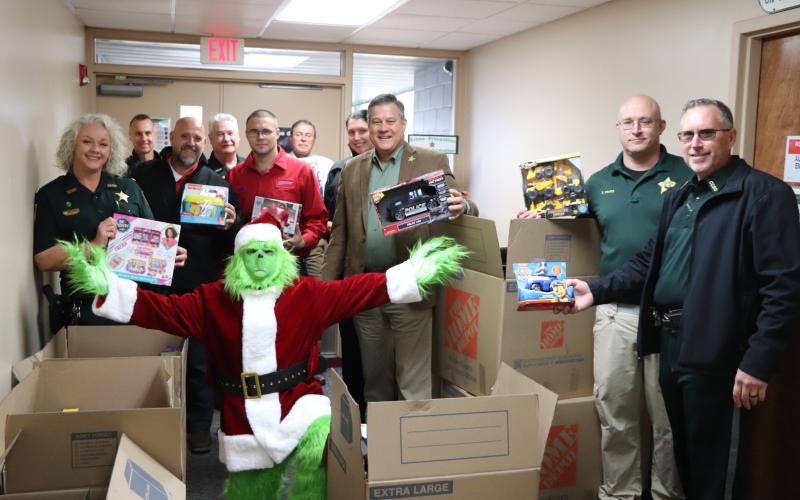 Eddie Medina, dressed as the Grinch, shows off the donated toys in front of Sheriff Mark Hunter (center) Wednesday morning at the Columbia County Sheriff’s Office. (COURTESY)