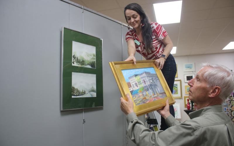Sheila Carr, Gateway Art Gallery Curator, is assisted by Jim Riley as she hangs artwork for the upcoming ‘The Art Of Matter’ exhibit which will be featured in the gallery during January. (TONY BRITT/Lake City Reporter)