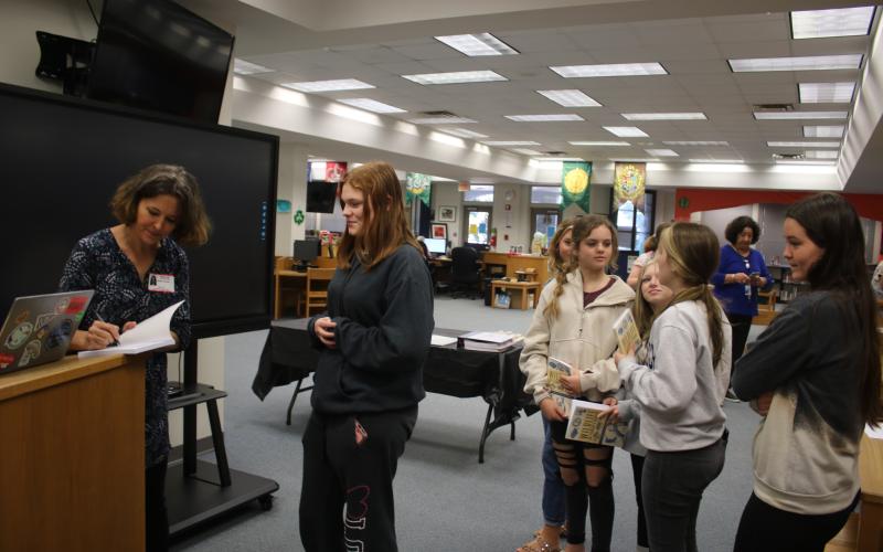 Sandra Poucher (from left) autographs a copy of her book, ‘Wildlife of Florida’s Springs,’ for Sanafa Sanders on Monday morning in the Fort White High School Media Center. (TONY BRITT/Lake City Reporter)