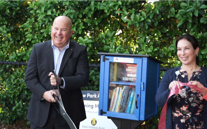 John Medina, president and CEO of First Federal Bank, cuts the ribbon on a Little Free Library at the Kiwanis Children’s Park adjacent to the bank’s headquarters on W. U.S. Highway 90 during a ceremony Thursday morning. Also pictured is Stephanie Esposito, the bank’s corporate marketing manager. (COURTESY)