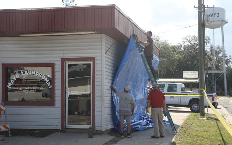 Mayo Laundromat owner Micah Hart staples a tarp to the outside of his business Tuesday afternoon after a semi crashed into the building, and pushed other vehicles through it, Tuesday morning. (MORGAN MCMULLEN/Lake City Reporter)
