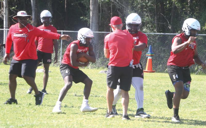 Fort White coach Demetric Jackson (left) hands the ball off to running back Maliki Clark (middle) during practice on May 1. (MORGAN MCMULLEN/Lake City Reporter)