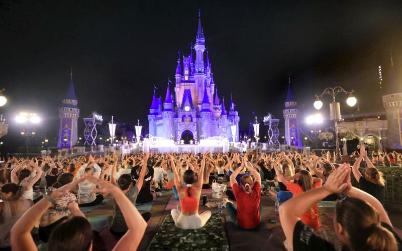 Walt Disney World cast members stretch at Cinderella Castle in a pre-dawn gathering during an annual team yoga session to commemorate International Yoga Day. (JOE BURBANK/Orlando Sentinel via AP)