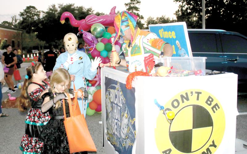 Xzailia Keown (from left), 8, checks her bag of candy as her sister, Nevaeh Keown, 9, gets candy from the DOT’s Crash Test Smarties during Tuesday night’s DOT Trunk or Treat event. (TONY BRITT/Lake City Reporter)