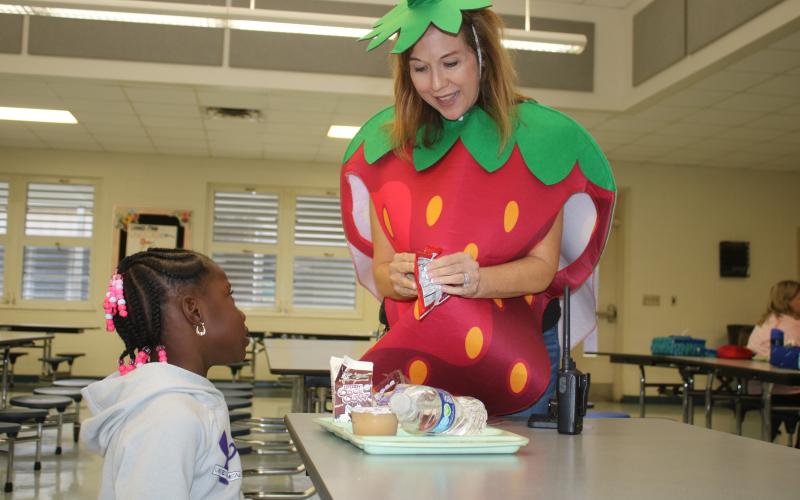 Westside Elementary School Principal Jennifer Saucer opens a carton of milk for a student Friday morning. Saucer was wearing the strawberry costume as part of National School Luncheon Week. (TONY BRITT/Lake City Reporter)