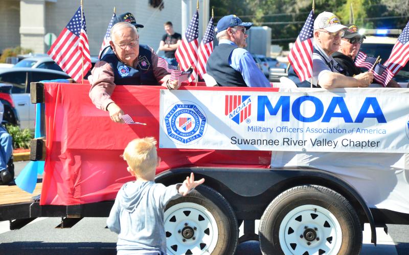 Vern Lloyd of Lake City hands a flag to a youngster who sprinted to catch up to the Military Officers Association of America float during the 2019 Veterans Day parade. (FILE)