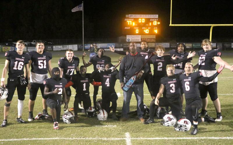 Fort White coach Demetric Jackson and the Indians’ seniors pose with the paddle after beating rival Santa Fe in the ‘Battle for the Paddle’ on Friday night. (MORGAN MCMULLEN/Lake City Reporter)