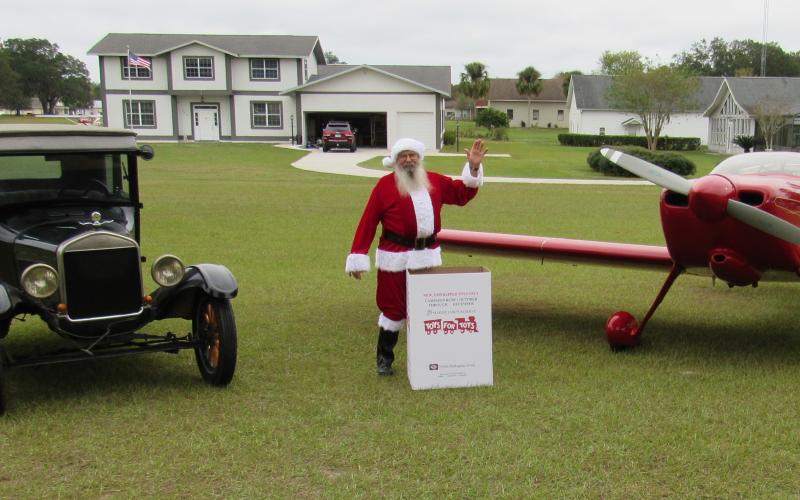 Mark Wiencek dresses as Santa next to a Cessna and a box of presents for Toys for Tots. (TONY BRITT/Lake City Reporter)