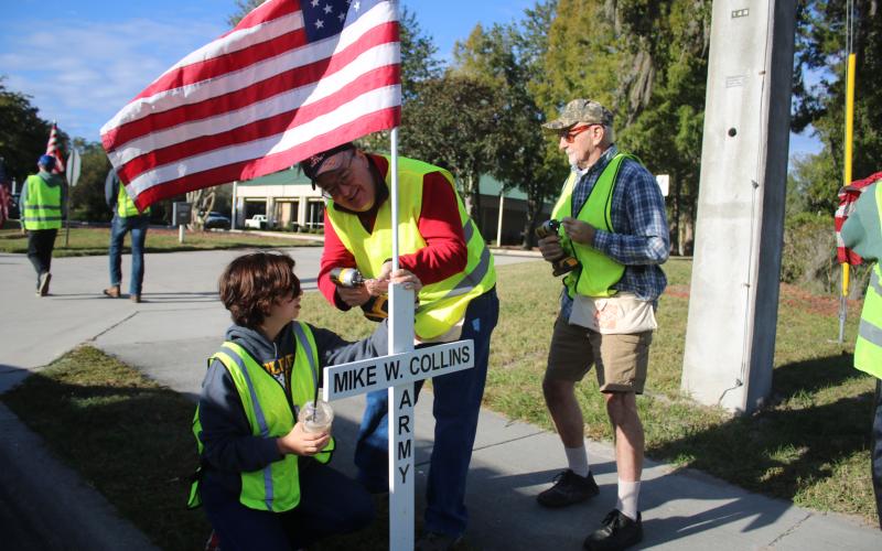 Mia Denney, a Columbia High School JROTC cadet holds an American flag as David Donovan drills it to a cross on Saturday morning. (TONY BRITT/Lake City Reporter)