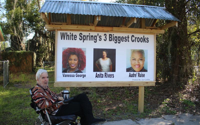 White Springs resident Joe Griffin sits in front of a sign erected on his property that calls Town Manager Vanessa George, Mayor Anita Rivers and Town Clerk Audre’ Ruise ‘crooks.’ (TONY BRITT/Lake City Reporter)