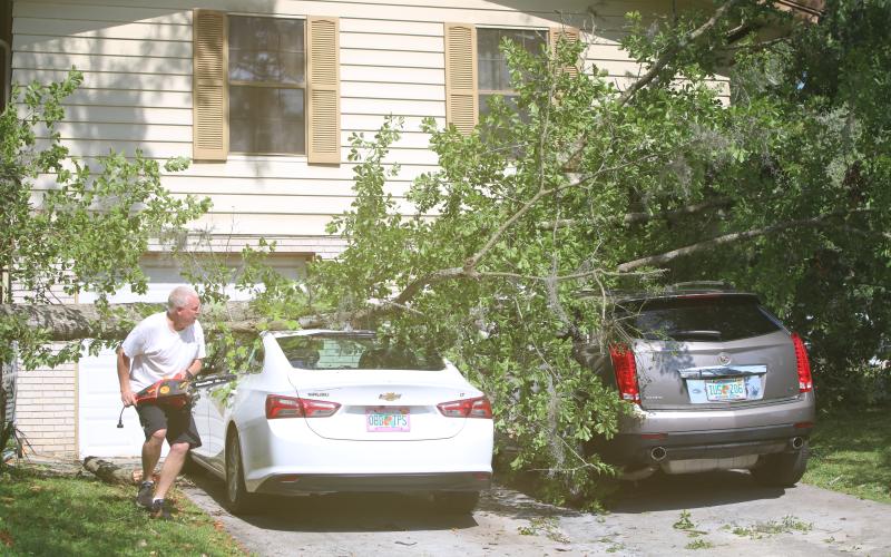 Wade Burlingame uses an electric chainsaw to cut a felled oak tree that landed across his vehicles at his Lake Montgomery Avenue home during Friday’s storm. (TONY BRITT/Lake City Reporter)