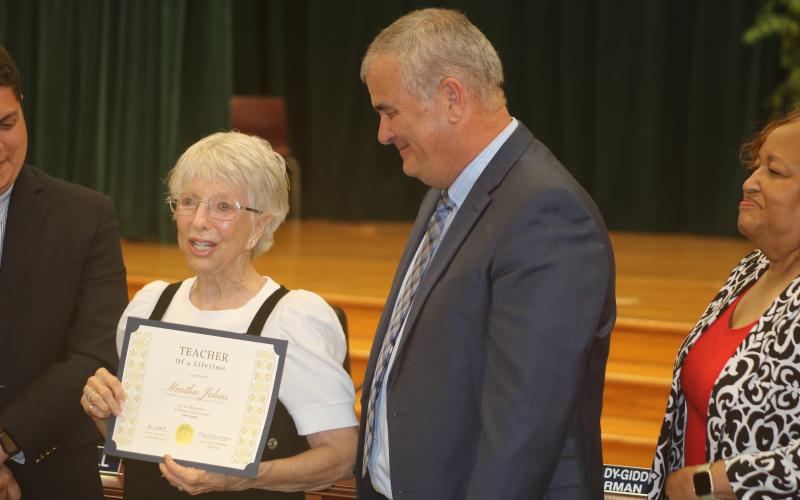 Martha Johns (from left) addresses the audience after getting her Teacher of a Lifetime certificate from Superintendent Lex Carswell on Tuesday evening. (TONY BRITT/Lake City Reporter)