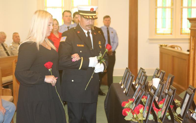 Julie Boozer, accompanied by Lt. Greg Sund, prepares to place a rose at the base of her father’s portrait during Tuesday’s Public Safety Memorial. Boozer’s father, Dwight, was Lake City’s assistant fire chief. (TONY BRITT/Lake City Reporter)