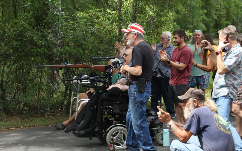 Pete Herrick, surrounded by friends and family, reacts after firing a breath-powered .308 rifle to set off a stack of cakes filled with Tannerite binary explosives Saturday during his ‘Alive Party.’ Herrick, a Fort White man, was seriously injured during Operation Iraqi Freedom 20 years ago today. (MORGAN MCMULLEN/Lake City Reporter)