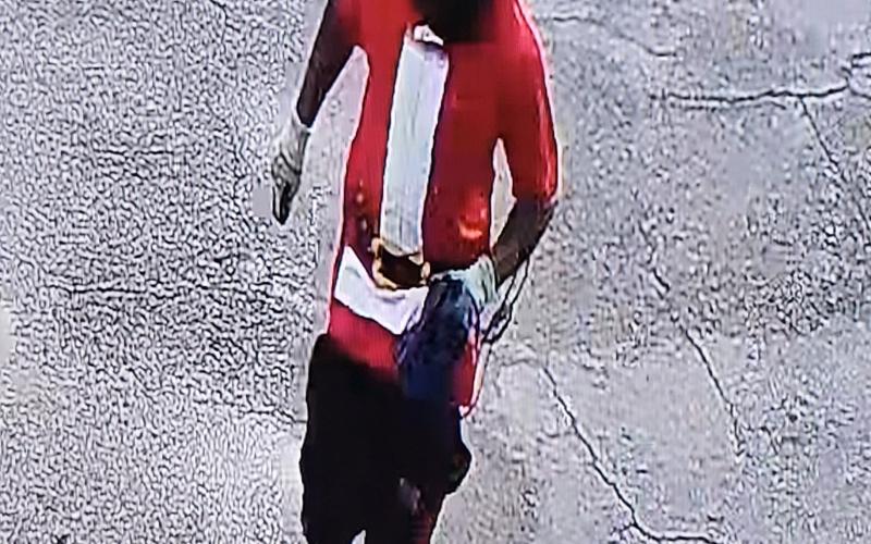 Gary Hollie, wearing a Halloween-style mask and a ‘Santa’ T-shirt, runs from the Dollar General on SW Main Boulevard after an armed robbery at the store on June 12. (COURTESY)