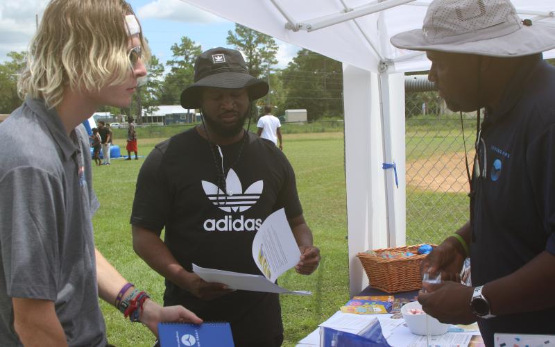 Samuel Jeter (from left) and Carlos Scippio collect information and school materials from Travis George at the Project Cope vendor booth during the inaugural Unity Community Day at Richardson Community Center. (TONY BRITT/Lake City Reporter)