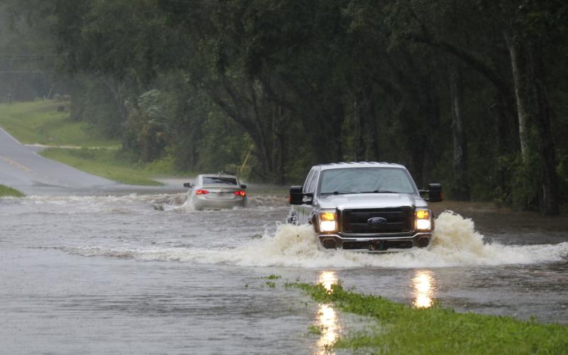 Vehicles drive through flood waters on County Road 240 east of Branford Highway (State Road 247) on Monday afternoon following Tropical Storm Debby. (JAMIE WACHTER/Lake City Reporter)