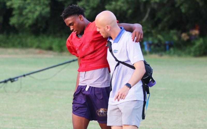 Columbia quarterback Xavier Collins walks off the practice field with the help of the team trainer after injuring his right knee on the final play of Monday’s practice. (JORDAN KROEGER/Lake City Reporter)