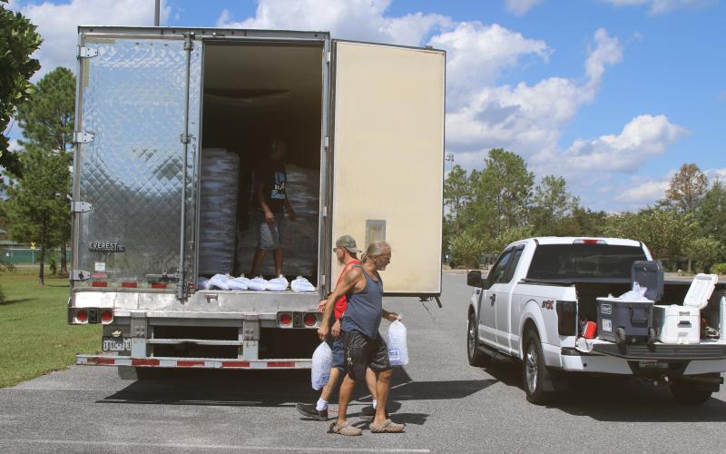 Tony Humphreys and Tony Dale, who live in a neighborhood off State Road 47, carry bags of ice from a trailer at the Southside Sports Complex to their truck on Sunday afternoon. (TONY BRITT/Lake City Reporter)