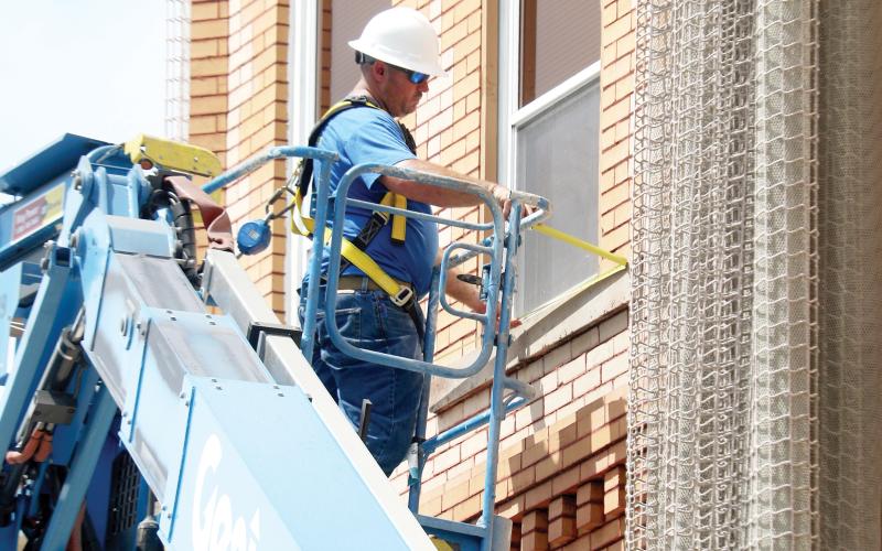 A worker measures a window on the outside of Lake City Hall on Tuesday as work begins to determine what is causing issues with the bricks on the historic building so the protective netting can be removed. (TONY BRITT/Lake City Reporter)