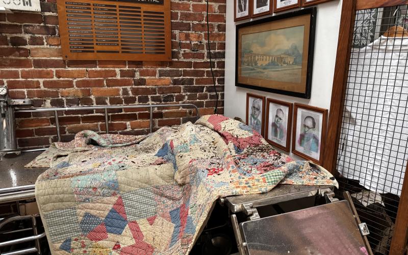 A quilt was laid out to dry Saturday following rain damage inside the Suwannee County Historical Museum after its roof was damaged during Hurricane Helene. Photos on the wall behind the quilt also show water damage. (JAMIE WACHTER/Lake City Reporter)