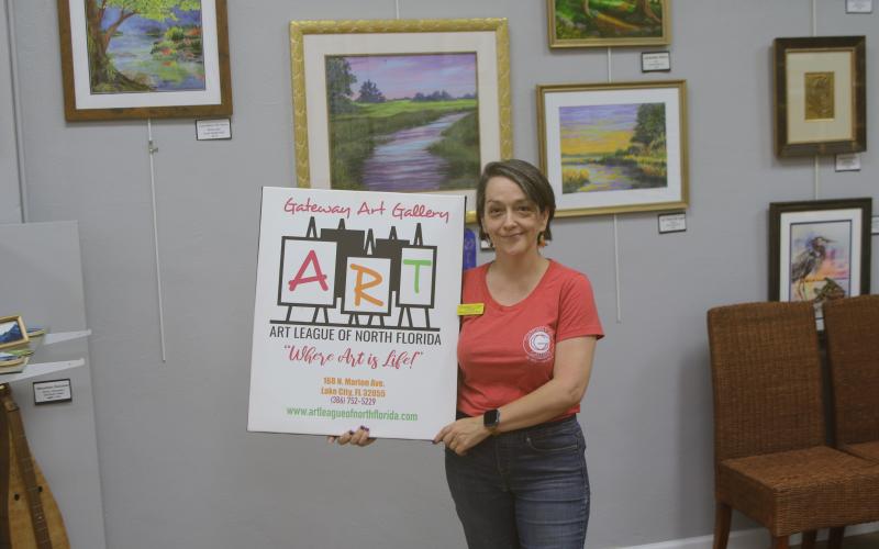 Sheila Carr, Gateway Art Gallery curator, is pictured with an Art League sign after they closed on purchasing their downtown building Thursday. (TONY BRITT/Lake City Reporter)