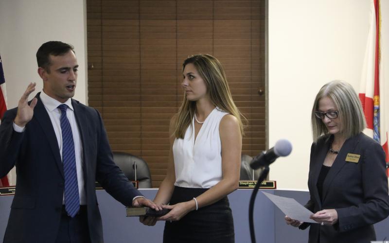 Lake City Mayor Noah Walker takes the oath of office Monday at the outset of the Lake City Council meeting as his wife, Chani, looks on while holding the Bible that he took the oath on. (MORGAN MCMULLEN/Lake City Reporter)