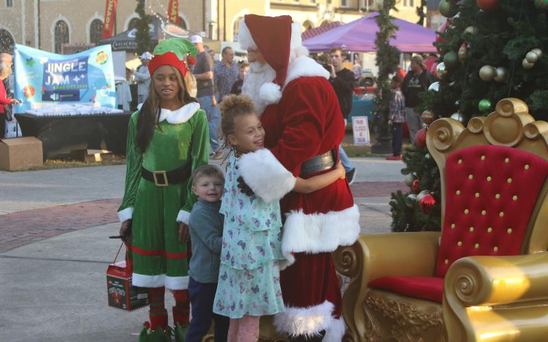 Santa Claus and one of his elves welcome a pair of children at the Christmas tree lighting  ceremony at Olustee Park Sunday night. (TONY BRITT/Lake City Reporter)