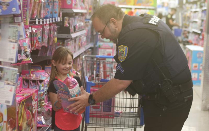 Paisley Daniels (left) is all smiles as she shows Lake City Police Department officer Brandon Rose an item she has selected for a Christmas gift, during LCPD’s Shop With A Cop event on Wednesday morning at Walmart. (TONY BRITT/Lake City Reporter)