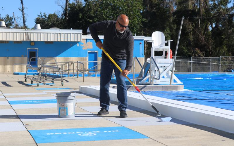Chris Cuadras, the new aquatic director for the Columbia County School District, applies some Cool Deck paint to the concrete around the pool Monday. (JAMIE WACHTER/Lake City Reporter)