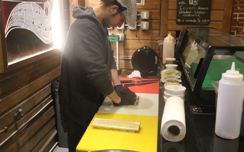 Tyler Hilton, a sushi chef at The Tavern, rolls up some sushi Friday afternoon as part of the Ribs and Rolls lunch special. Among that lunch menu is the Cowboy Roll, which is made with brisket, cream cheese, barbecue sauce and green Sriracha and then is deep fried. (MORGAN MCMULLEN/Lake City Reporter)