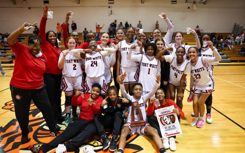 The Fort White girls basketball team celebrates with the District 6-R trophy after defeating Trenton on Saturday night. (JACK HOWDESHELL/Lake City Reporter)