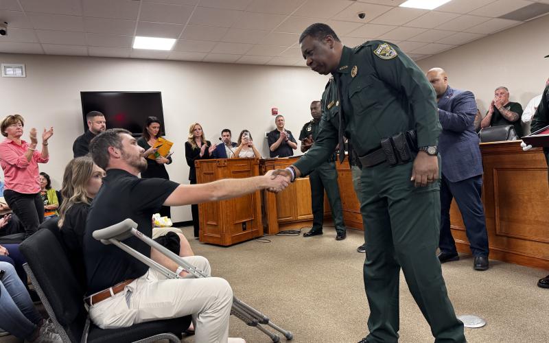 Suwannee County Deputy Justin Dalton, shot and injured in a chase of a murder suspect Friday morning, shakes hands with Gadsden County Sheriff Morris Young. Young and Suwannee County legislators, Sen. Corey Simon and Rep. Jason Shoaf, honored Dalton on Monday with a state flag that flew over the Florida Capitol on Friday. (JAMIE WACHTER/Lake City Reporter)
