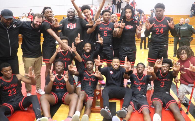 Fort White’s boys basketball players and coaches hold up their Ls after earning a trip to Lakeland with a 54-51 win over Hilliard in the Region 3-R championship on Tuesday. (MORGAN MCMULLEN/Lake City Reporter)