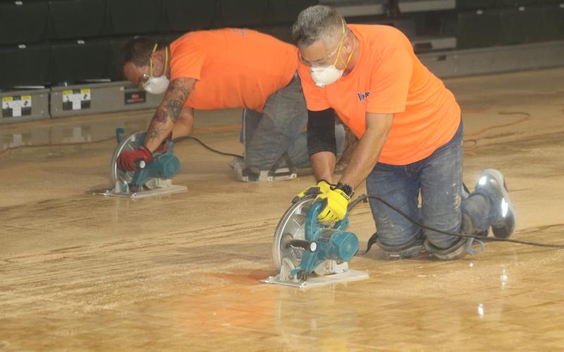 Frank Roque (foreground) and Corey Watkins of Impact Sport Surfaces Inc., use saws to cut FGC’s old parquet basketball court. (TONY BRITT/Lake City Reporter)