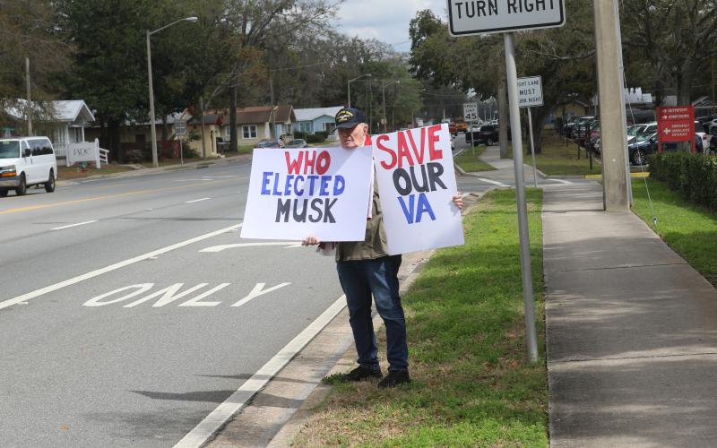 Charles Trowbridge, a U.S. Navy veteran and Fort White resident, holds up signs outside the Lake City VA Medical Center on Monday protesting the Department of Government Efficiency’s planned cutting of 80,000 Veterans Affairs employees. (TONY BRITT/Lake City Reporter)