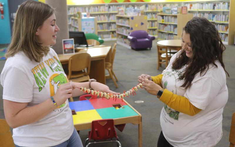 Kate Duong (from left), Columbia County Public Library assistant director, and Andrea Sirard, Columbia County Youth Services librarian, work on creating an edible spinal column made of cereal and candy. (TONY BRITT/Lake City Reporter)