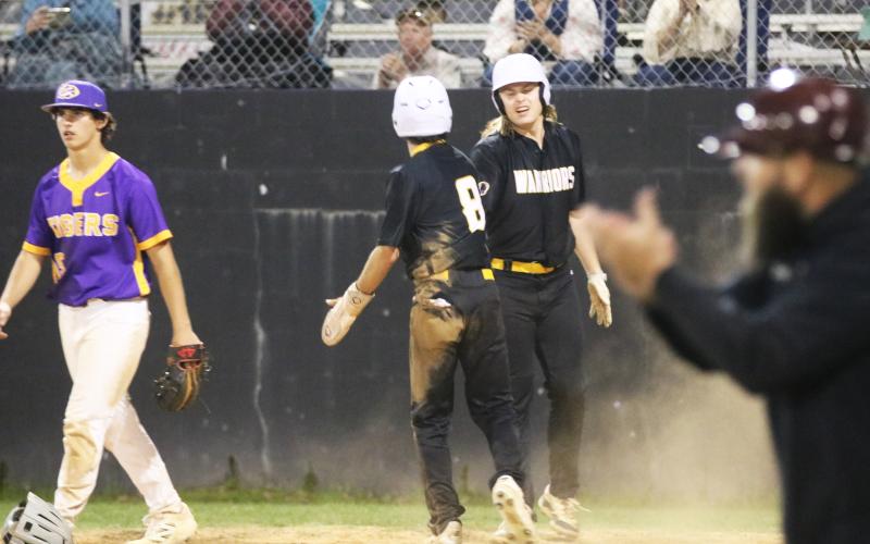 West Nassau's Owen Layfield (8) celebrates with David Treadwell after scoring the go-ahead run in the sixth inning as Columbia pitcher Goose Lord walks back to the mound Wednesday night. (JORDAN KROEGER/Lake City Reporter)