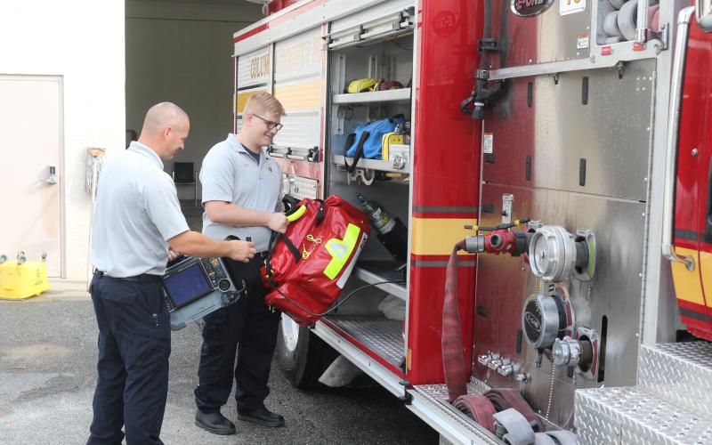 Columbia County Fire Rescue employee Jake Doyle (left) holds a cardiac monitor as Justin Ingle loads an Advanced Life Saving bag onto a fire engine at Station 43 on Friday morning. (TONY BRITT/Lake City Reporter)