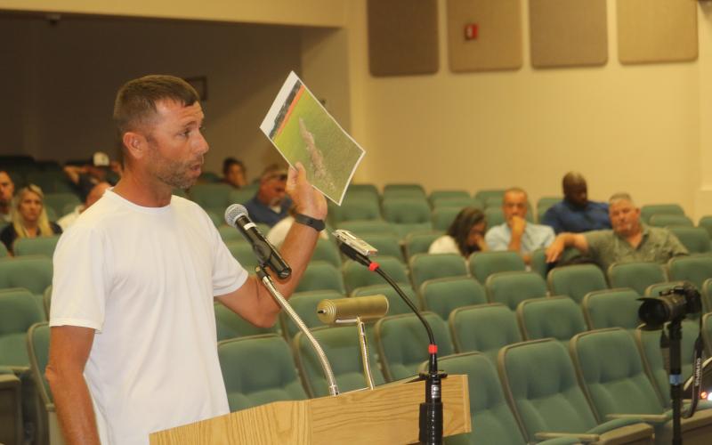Bobby Griffis shows county commissioners a picture of damage to a local field during Thursday evening’s county commission meeting as several citizens attended the meeting opposing the plan to raise field usage fees for travel ball teams. (TONY BRITT/Lake City Reporter)