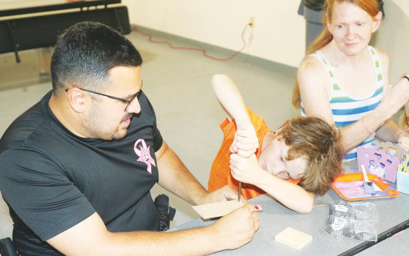 Columbia County School Resource Deputy Tony Geurra helps Negan Barker, 8, with his wood working skills. (TONY BRITTLake City Reporter)