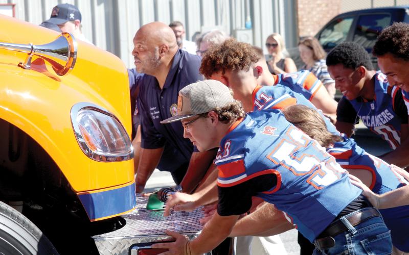 Sen. Corey Simon (left) is joined by seniors on the Branford football team Tuesday morning in pushing in the Branford Volunteer Fire Department’s new engine, which was obtained with state funding. The truck is painted orange and blue to match the colors of Branford High School. (JAMIE WACHTER/Lake City Reporter)