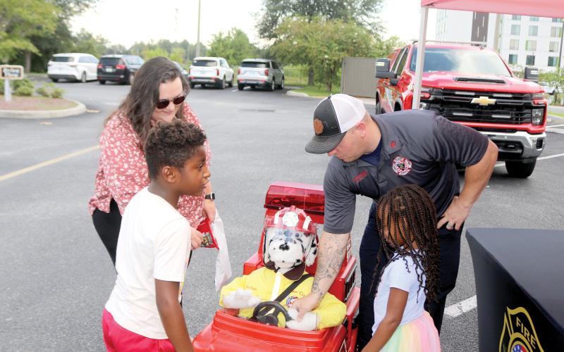 Elias Flores (clockwise from left), 6, Chelsea Flores, Lake City Firefighter Dustin Alford and Ava Flores, 4, play with Patches, a fire department remote controlled vehicle during the Fire Rescue N’ Cones event on Monday. (TONY BRITT/Lake City Reporter)