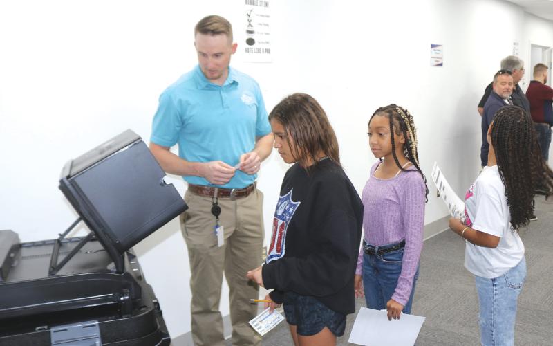 Kent Banner (left), Columbia County Assistant Supervisor of Elections, helps fifth-grade Eastside Elementary School students place their ballots into the tabulator on Tuesday morning during a school election at the county election’s office. (TONY BRITT)