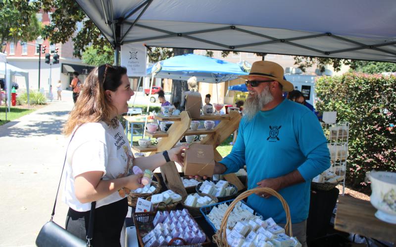 A shopper at a previous market event in downtown Olustee Park buys soap from the Kinghorn Farms booth. The City of Lake City’s Growers and Makers Market returns downtown Saturday. (FILE)